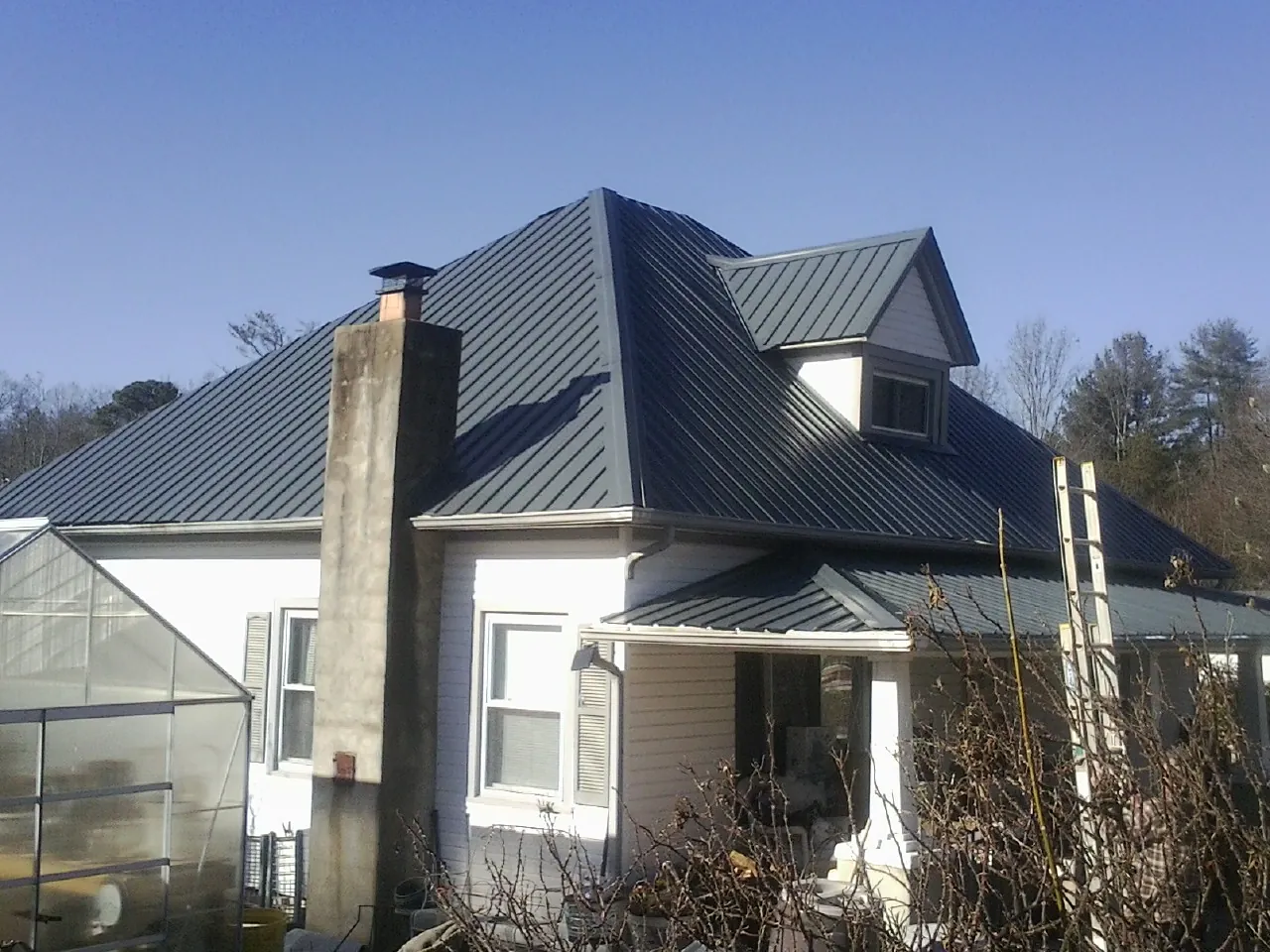 Dark blue standing seam metal roof on a white farmhouse with dormer — Slate & Tile Roof Repair by Roofing Brothers in Black Hawk