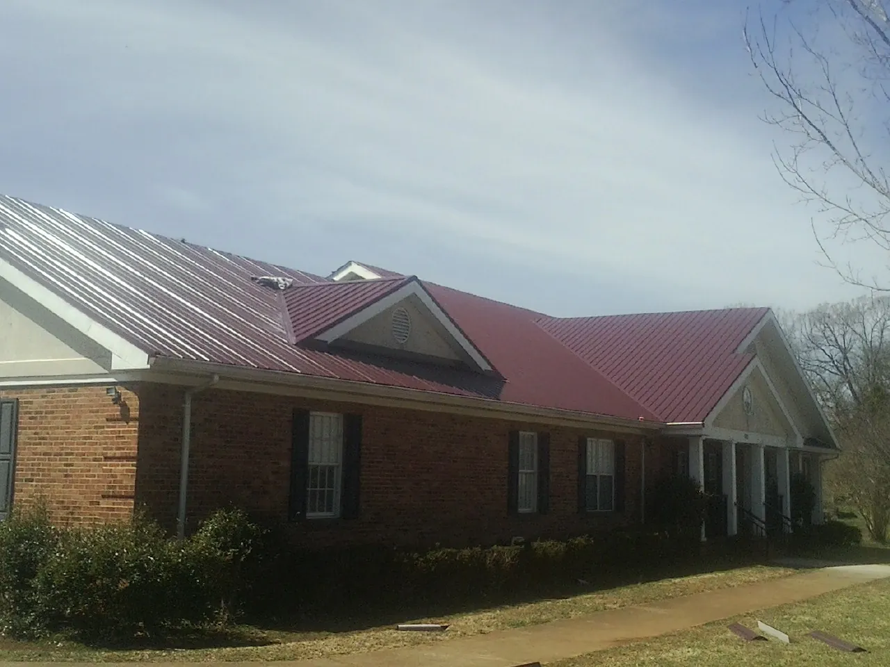 Red metal roof with gabled entries on a long brick building, from a Hail Damage Roof Repair job in Black Hawk