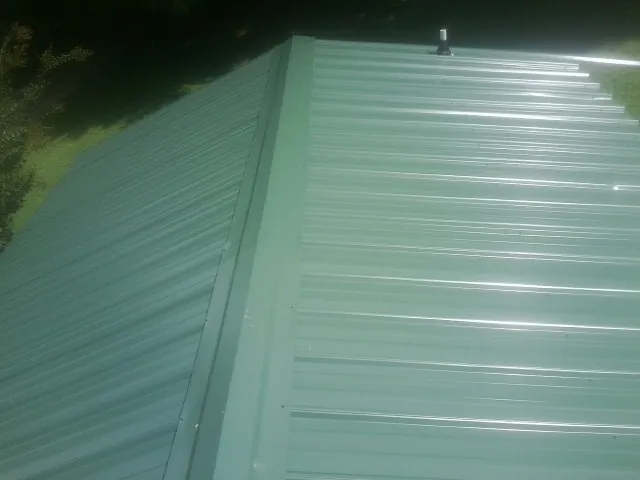 New green metal panels meeting at the ridge of a roof — Flat Roof Repair work by our crew in Black Hawk