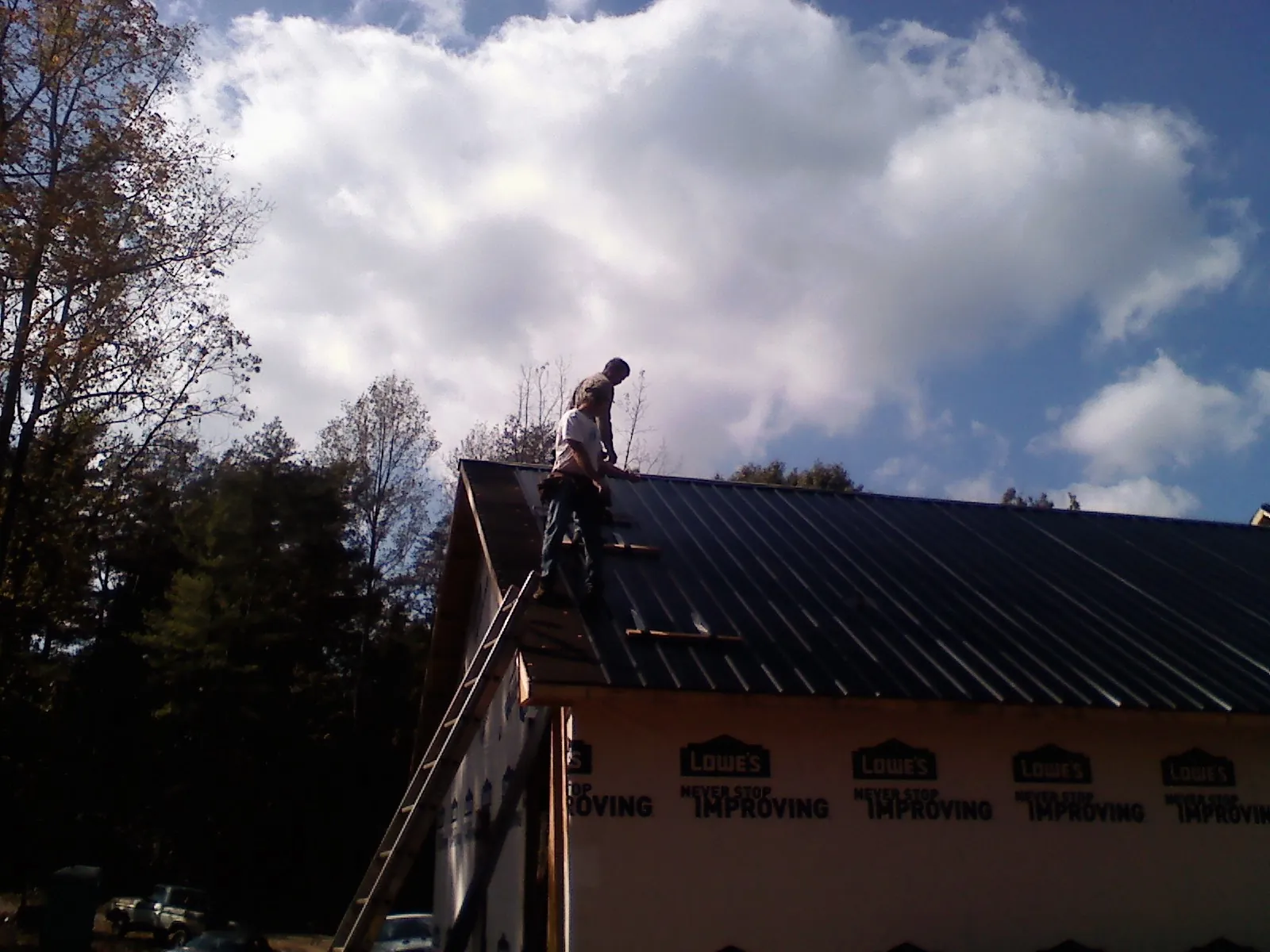 Roofer fastening dark metal panels high against a cloudy sky, from a Roof Inspection job in Black Hawk