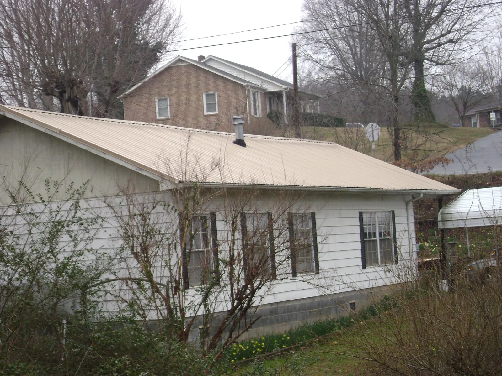 Tan metal roof on a white sided house set into a hillside — Commercial Roofing by Roofing Brothers in Black Hawk