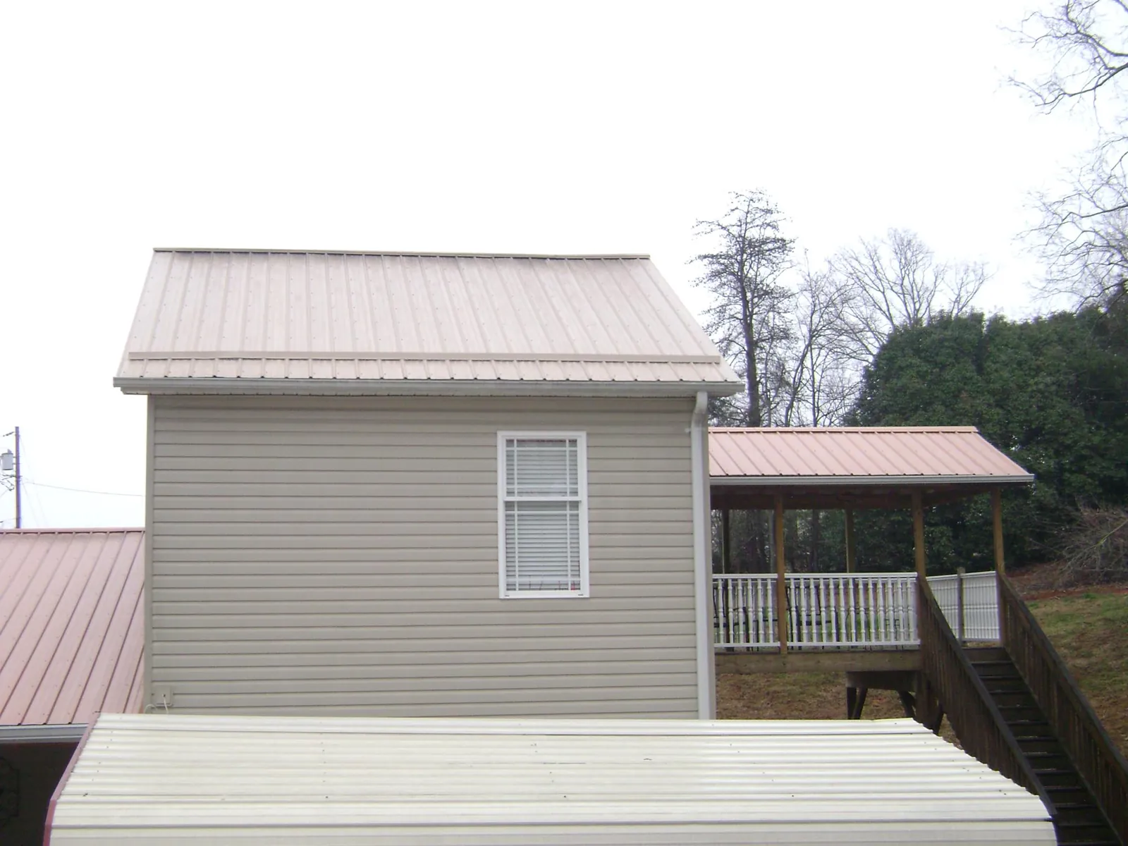 Tan metal roofs on a two story addition and attached porch, from a Roof Replacement job in Black Hawk